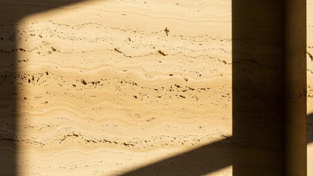 Parete in travertino con luce radente e ombre diagonali, materia viva e ritmo del tempo – architetto specchio Bolzano